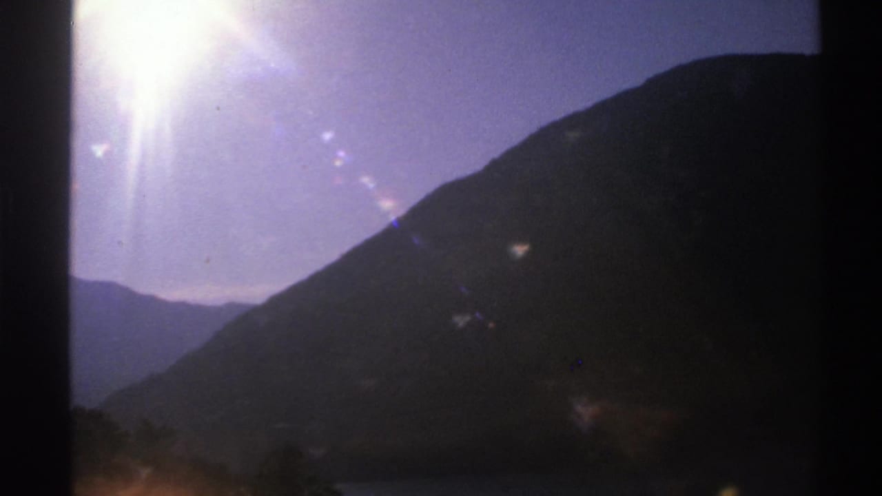 Dark mountain silhouette seen through a moving car window with bright sun flare in the sky.