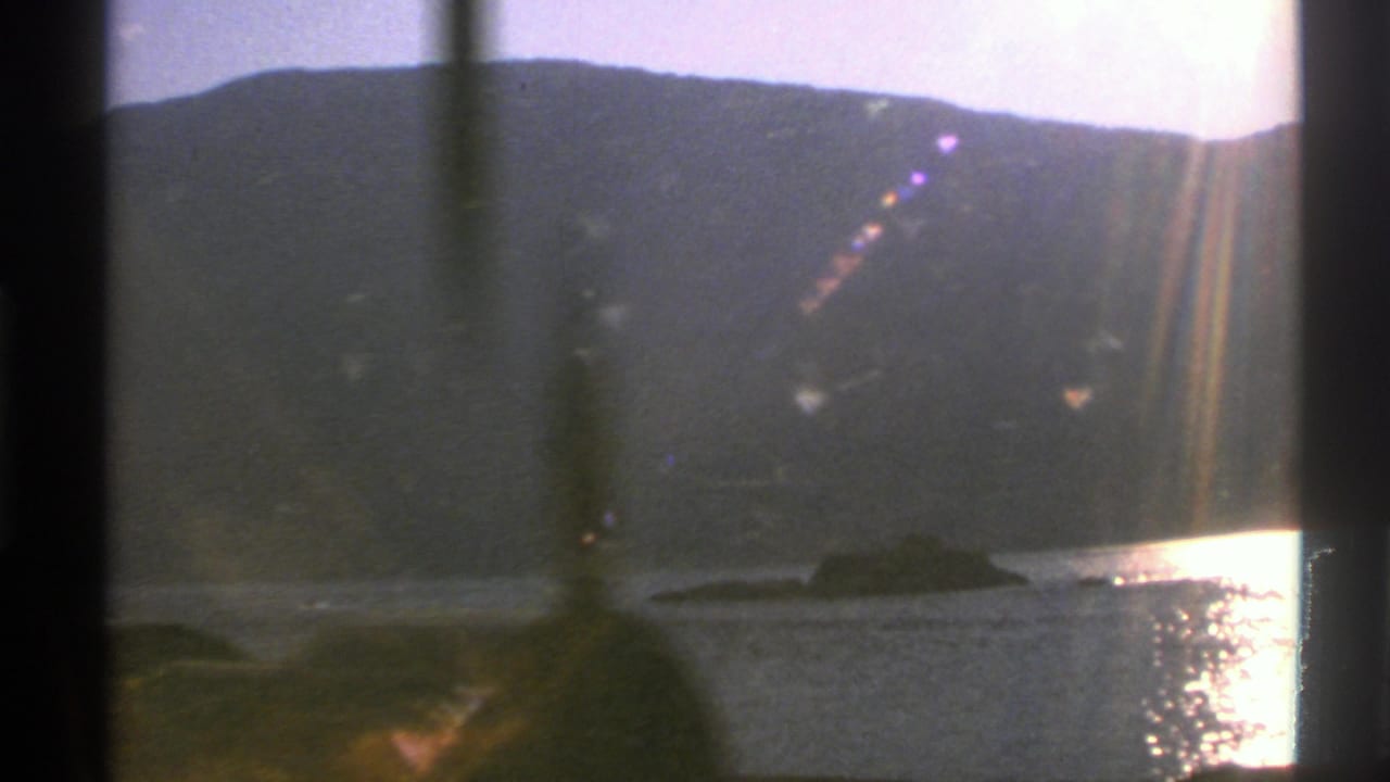 1976 Norway travel frame with a mountain lake, bright sunset reflection, window framing, and flare on 8mm film.