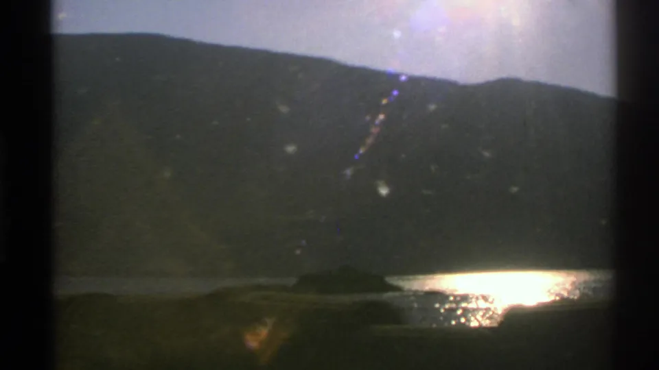 Norway 1976 8mm frame looking from a train across a lake toward a shadowed mountain ridge at dusk.