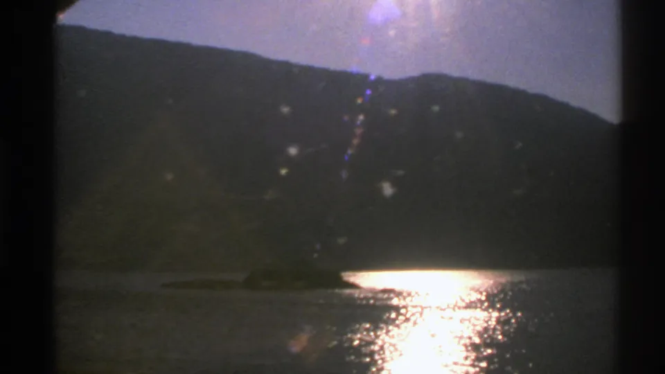 Final 1976 Norway travel frame showing a bright lake reflection, dark mountain slope, and train-window obstruction.