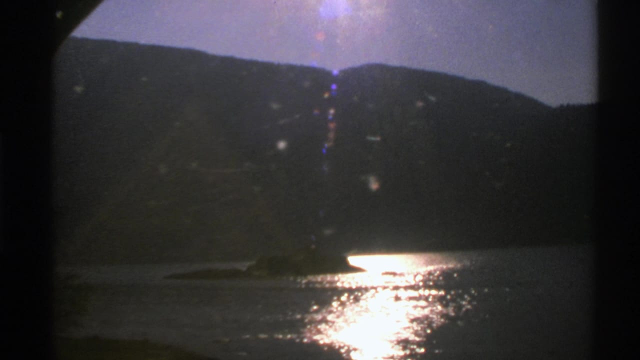 1976 Norway 8mm frame with a dark hillside above a lake, bright reflected sunlight, and visible film-frame borders.