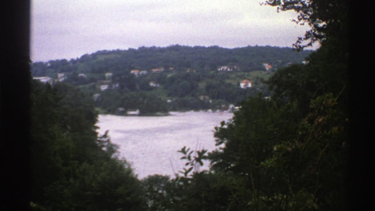 Lake, wooded hillside, and distant houses framed by trees.