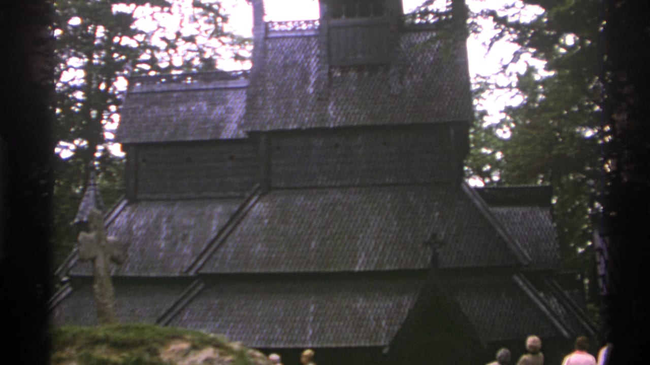 Wooden church facade and rooflines framed by trees, with several visitors visible along the bottom.