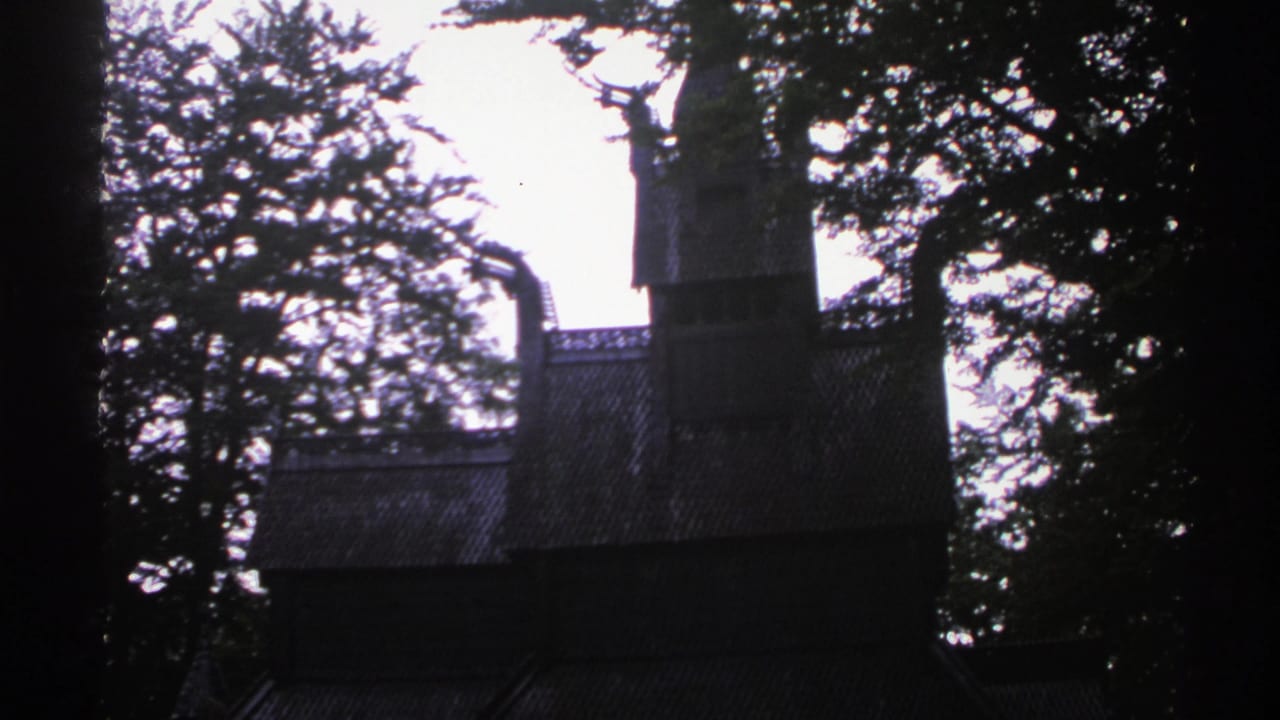 1976 Norway 8mm frame with a tall wooden tower, sloped roof, and surrounding trees in low light.