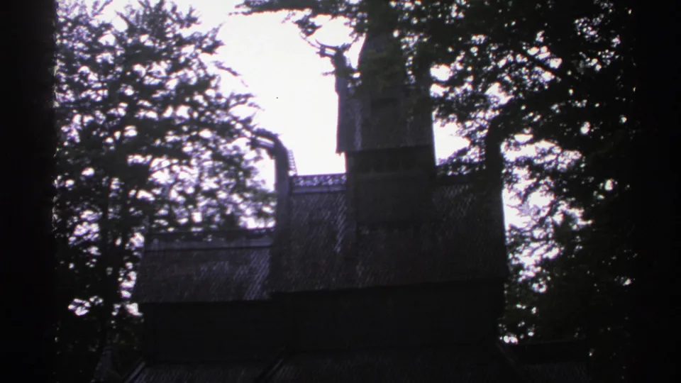 1976 Norway 8mm frame with a tall wooden tower, sloped roof, and surrounding trees in low light.