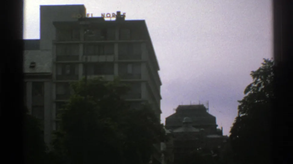1976 Norway frame showing a building with a Hotel Norge roof sign, trees, and another structure in the distance.