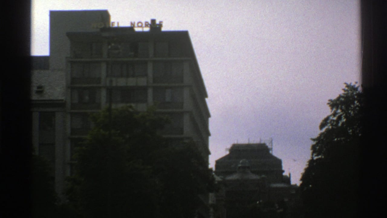 Modern hotel building with rooftop HOTEL NORGE sign under a cloudy sky, framed by dark window edges.