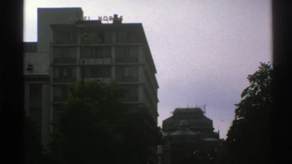 1976 8mm Norway footage showing a modern hotel facade with rooftop HOTEL NORGE sign, trees below, and a pale overcast sky.