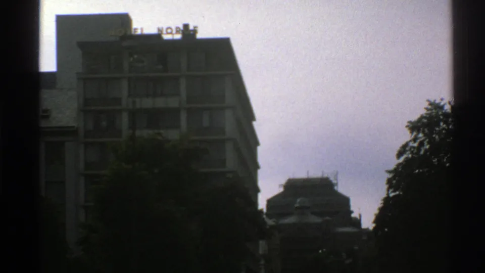 1976 Norway 8mm frame holding on a modern city hotel with visible HOTEL NORGE rooftop sign and tree cover below.