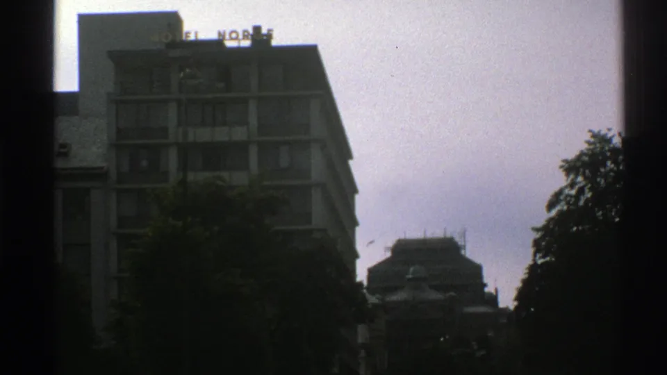 Late clip frame from 1976 Norway footage showing the HOTEL NORGE building through a window-like frame on a cloudy day.