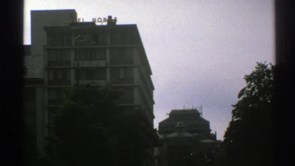 1976 Norway street-view frame with Hotel Norge signage, balconies, cloudy sky, and trees partly obscuring the building.