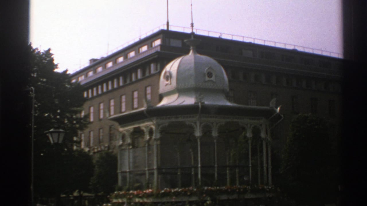 White domed pavilion in front of a large brick building with trees and a lamppost.