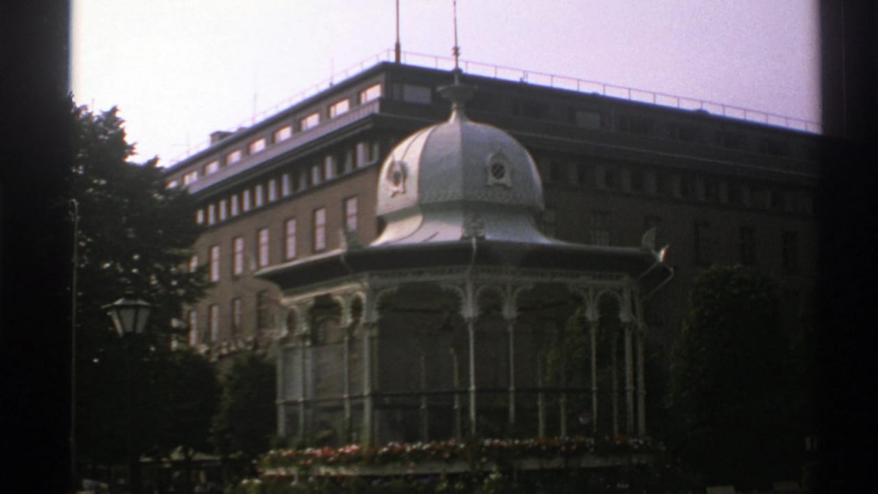 Domed pavilion and brick building seen through trees with dark film borders.