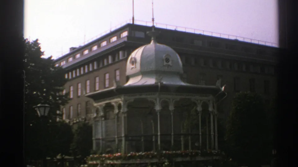 1976 Norway 8mm frame showing a slightly closer view of the ornate pavilion, flower bed, trees, and brick building behind.