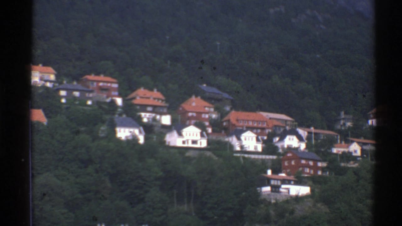1976 Norway 8mm frame showing a forested hillside with scattered white houses, red roofs, and darker buildings.