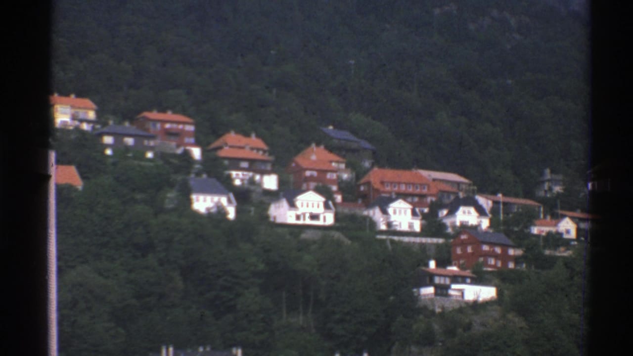Norwegian hillside houses sit among thick trees, with red roofs and white facades visible in the 8mm frame.