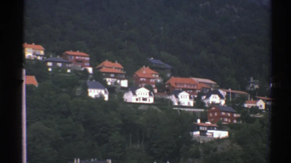 Norwegian hillside houses sit among thick trees, with red roofs and white facades visible in the 8mm frame.