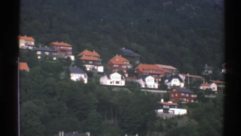 Final 8mm frame of the Norwegian hillside settlement, with clustered white houses and red roofs surrounded by forest.