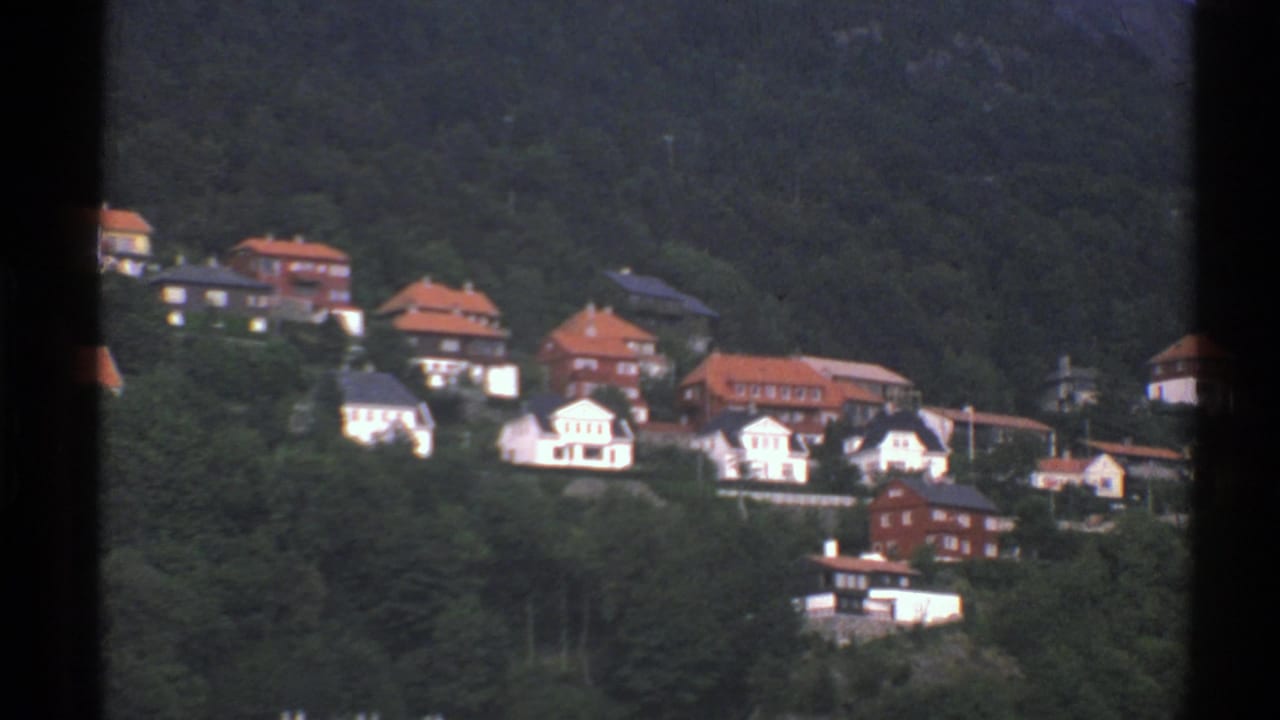 Residential hillside with red-roofed houses and trees.
