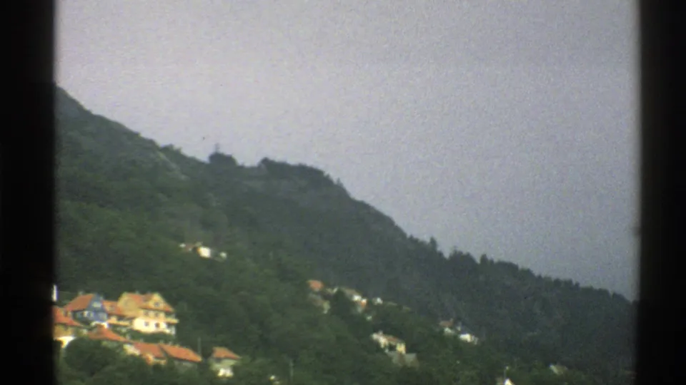 A softer 1976 Norway 8mm view of scattered hillside homes below a pale sky and wooded ridge.