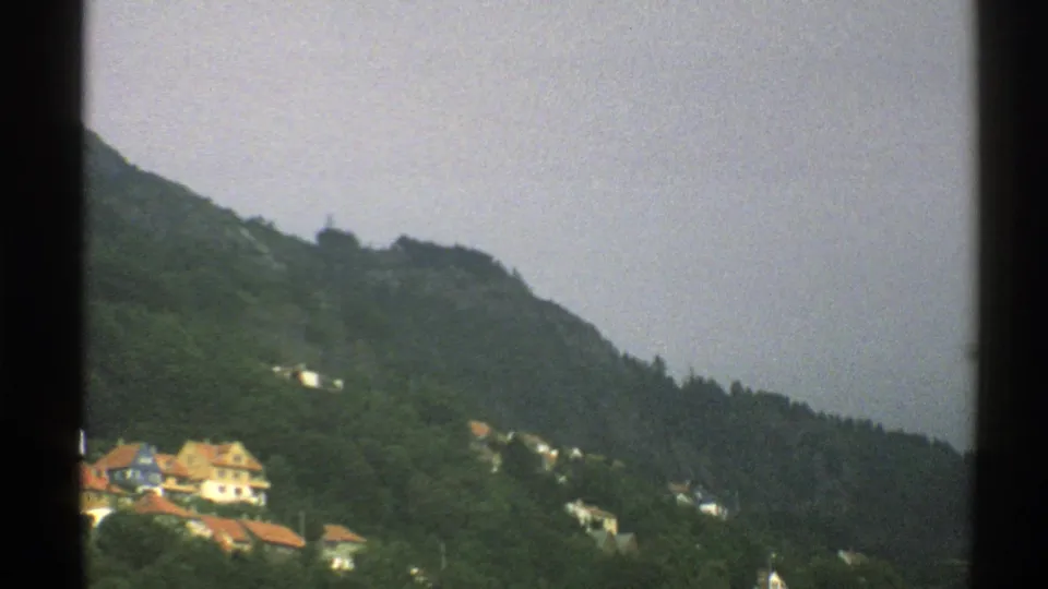 1976 Norway 8mm frame showing pale houses with red roofs on a green hillside beneath an overcast sky.