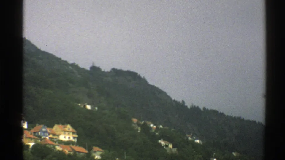 The final 8mm frame keeps the Norwegian hillside and small distant homes in view, with muted color and visible film grain.