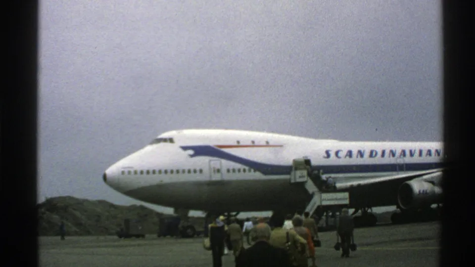 Norway 1976 frame of a Scandinavian Airlines Boeing 747 parked on the tarmac as passengers gather near mobile boarding stairs.