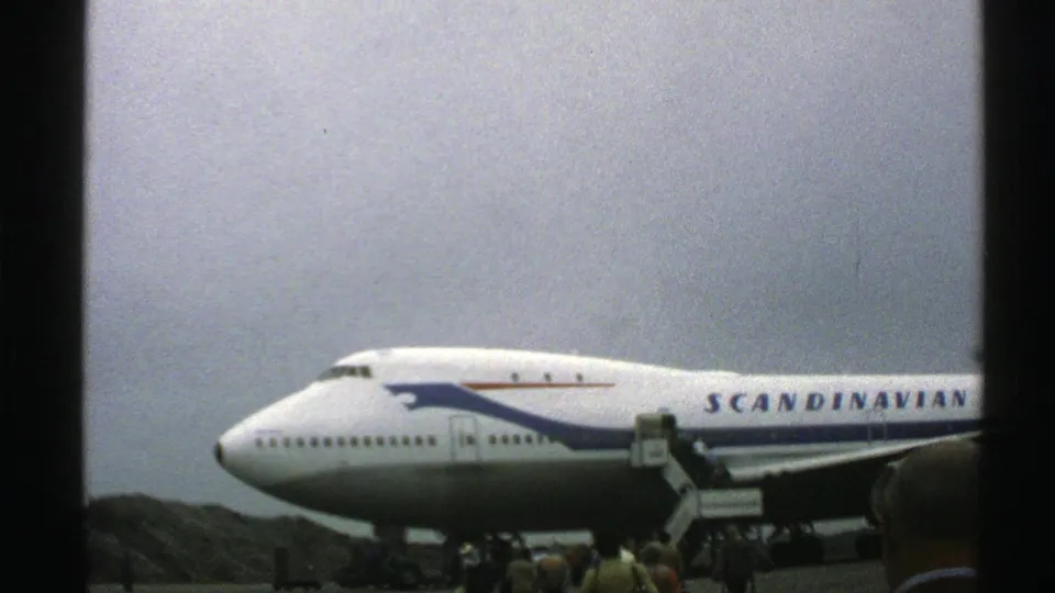 Norway 1976 8mm frame showing the nose and fuselage of a Scandinavian Airlines Boeing 747 with passengers boarding by mobile stairs.