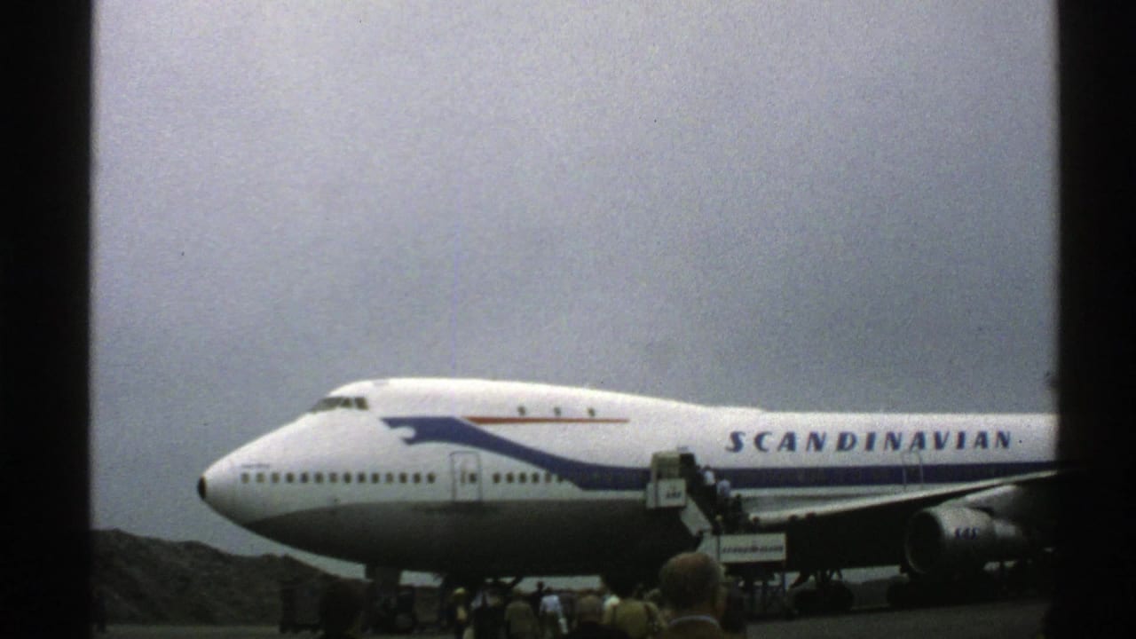1976 Norway 8mm frame showing a Scandinavian Airlines 747 at a small airport with boarding stairs and passengers near the fuselage.