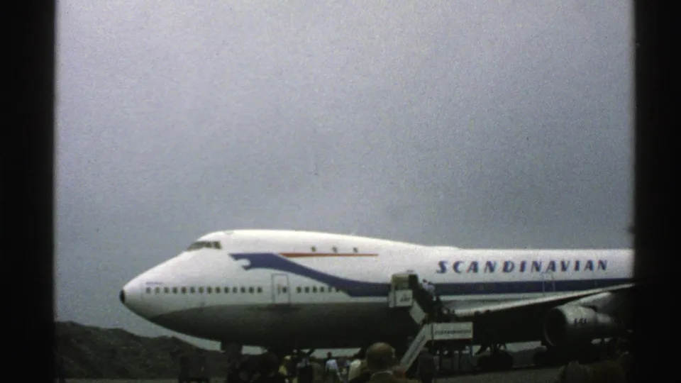 A Scandinavian Airlines 747 is seen in profile at a Norwegian airport, with mobile stairs positioned at the cabin door.