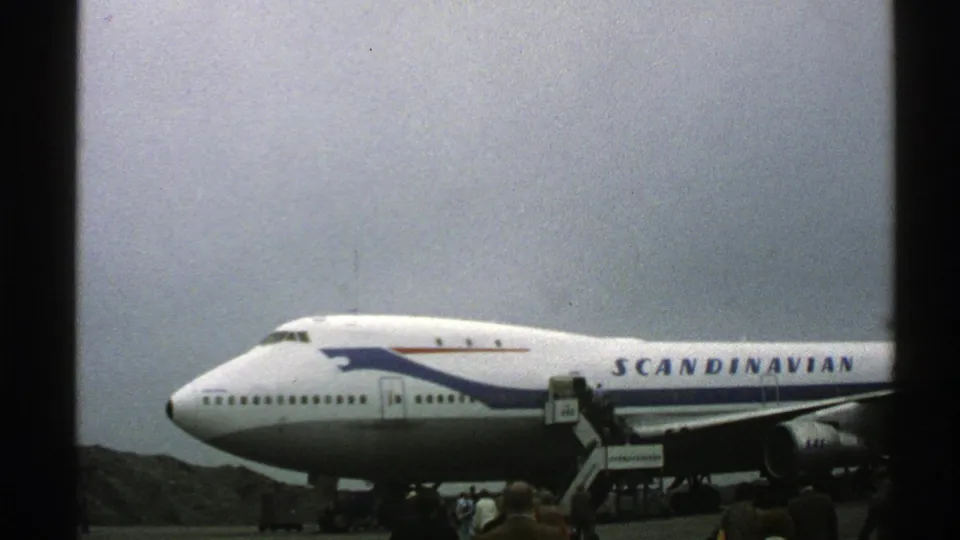 The large Scandinavian Airlines aircraft fills the frame as passengers cluster near the stairs under an overcast sky.