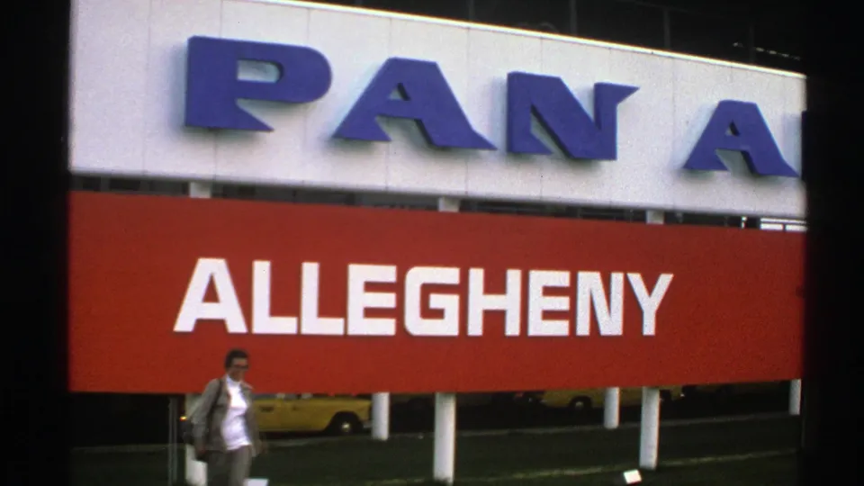 A woman in a light jacket crosses the lower frame beneath partial Pan Am lettering and the large red Allegheny sign.