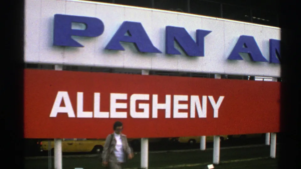 Near the end of the clip, the woman passes under the airline signs while the red Allegheny panel dominates the frame.