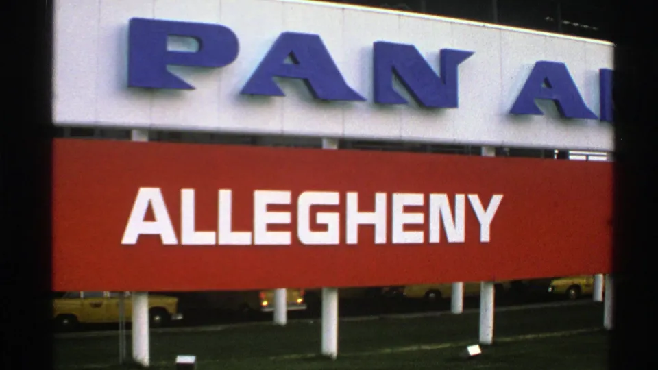 1976 Norway 8mm frame showing airport airline signage, white supports, and yellow taxis visible beyond the red Allegheny panel.