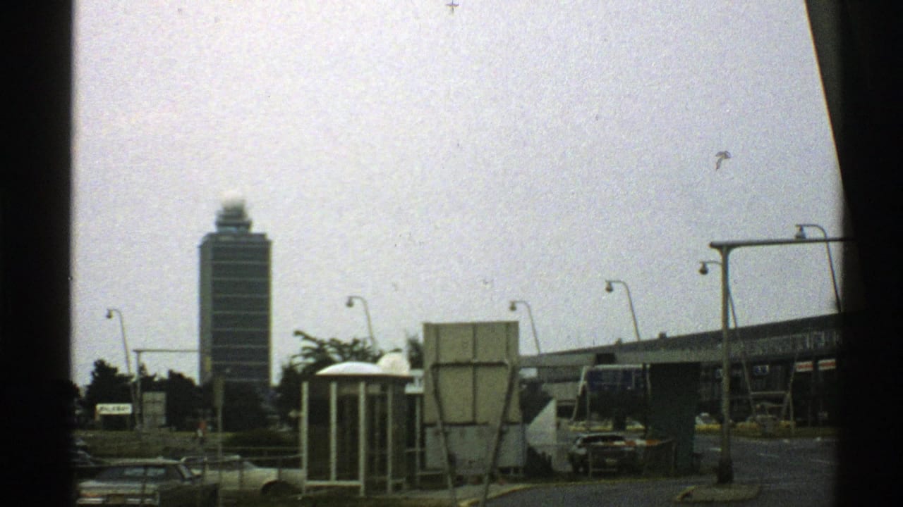 Tall tower seen past streetlights, cars, roadside structures, and dark frame edge.