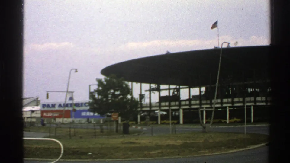 1976 Norway 8mm frame showing a large circular modern building, Pan American signage, a flag, and roadside grass.
