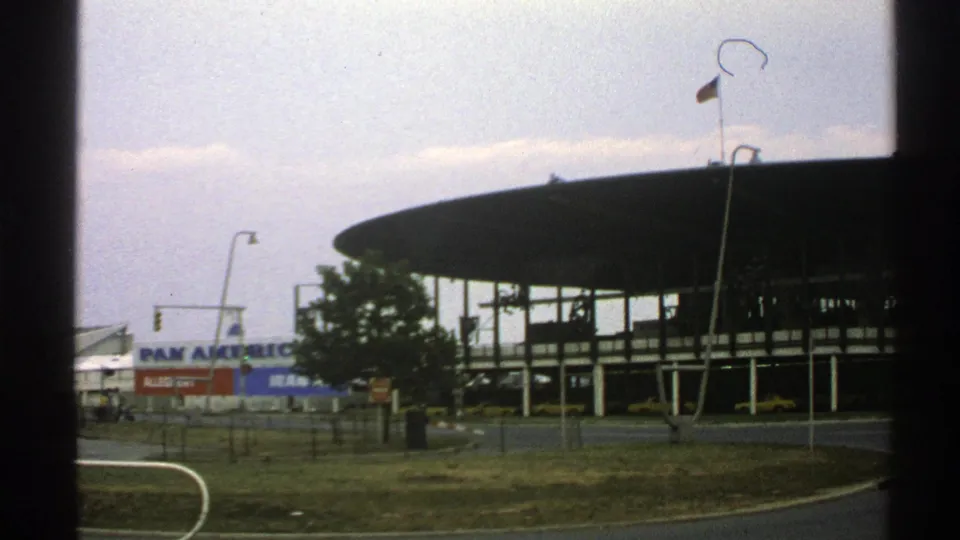 A 1976 Norway moving-vehicle frame shows the circular building, Pan American branding, flagpole, road, and cloudy sky.