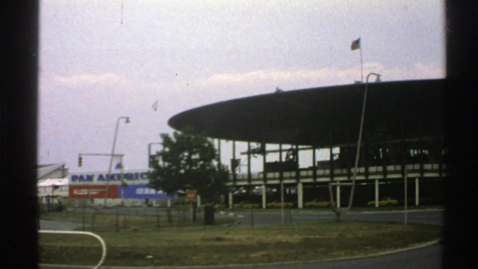 1976 Norway 8mm view of a modernist airport terminal with a circular roof, Pan Am sign, flagpole, roadway, and dark window-frame borders.