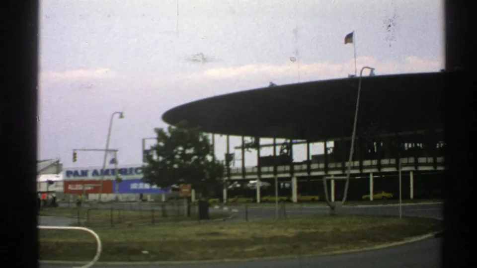 1976 Norway airport exterior with a round-roof terminal, visible Pan Am sign, flagpole, streetlights, road edge, and grassy foreground.