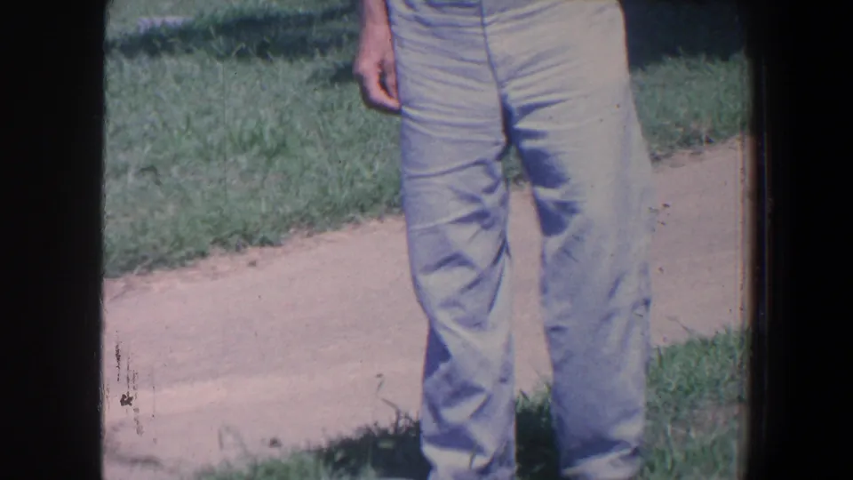 1959 Iowa 8mm frame showing a cropped man in light trousers standing near grass and a cemetery walkway.