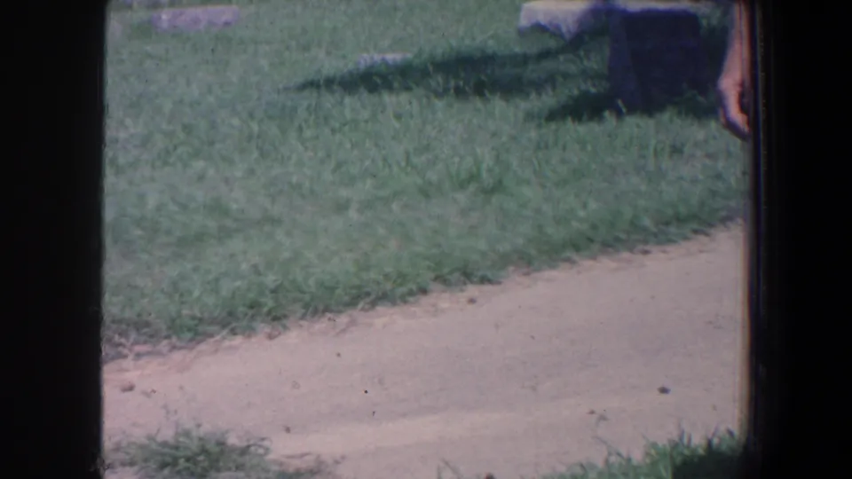 Cemetery grass and walkway in Iowa, 1959, with only the edge of a standing person visible at right.
