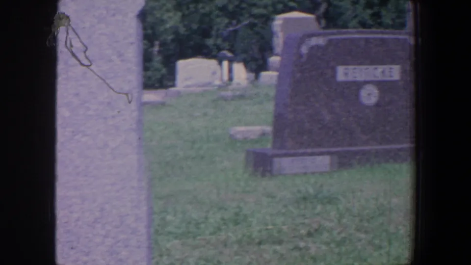 A REINCKE gravestone stands in a grassy Iowa cemetery, with a tall pale marker and other headstones behind it.