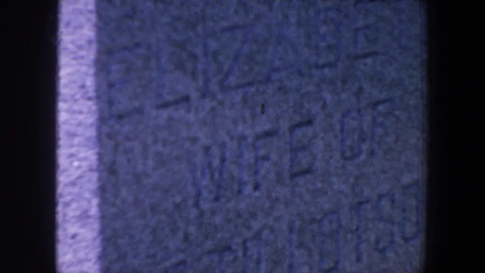 A tight 8mm close-up shows blue-toned stone texture and carved grave inscription details, partly difficult to read.