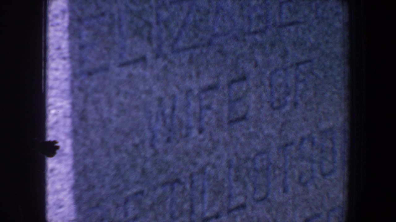 Close 1959 Iowa 8mm view of a worn gravestone face with partial carved text and dark film edges.