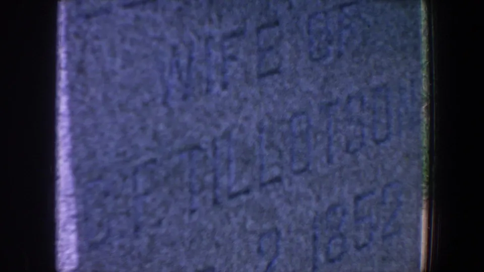 1959 Iowa home-movie close-up showing partial Elizabeth inscription and weathered carved dates on a gravestone.