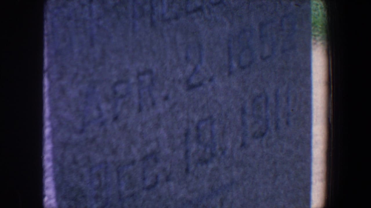 Close, soft view of a weathered tombstone surface beside dark film-gate borders.