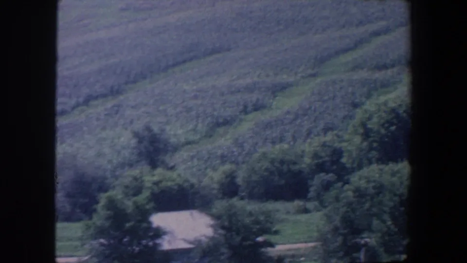 1959 Iowa rural 8mm frame showing farmland, trees, and a small light-roofed structure at the lower edge.