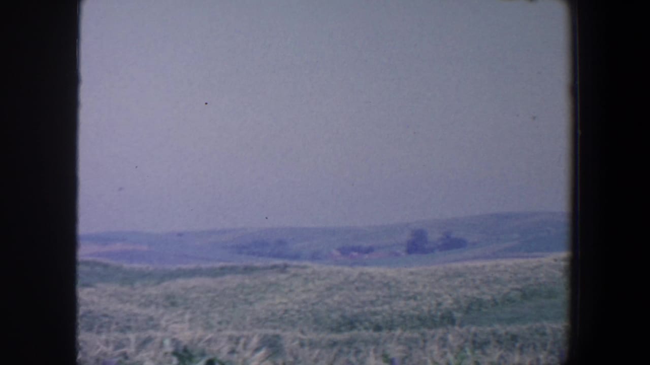 Distant low hills beyond a pale field, seen through dark vertical frame borders.