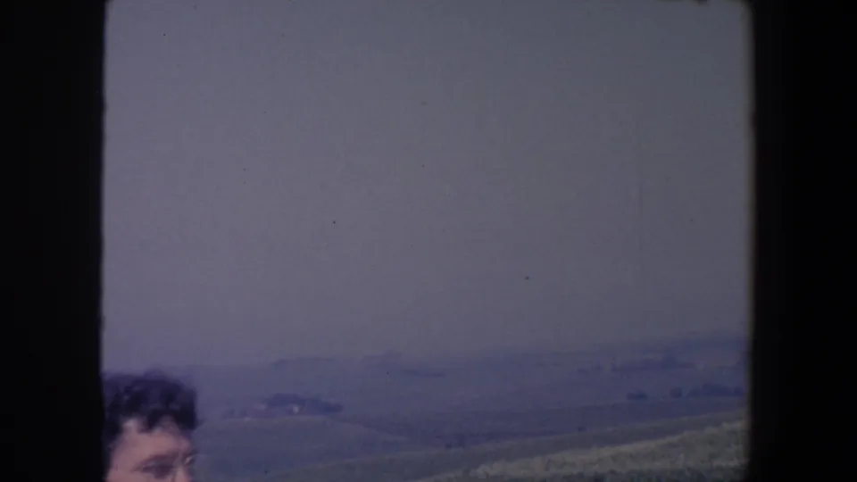 A partly visible woman appears at the lower edge of a 1959 Iowa hillside view across muted farmland and low hills.