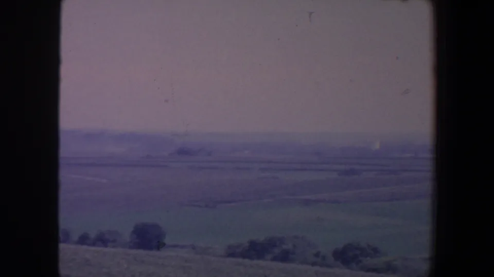 1959 Iowa home-movie frame with distant farmland, low tree clusters and muted color from the 8mm scan.